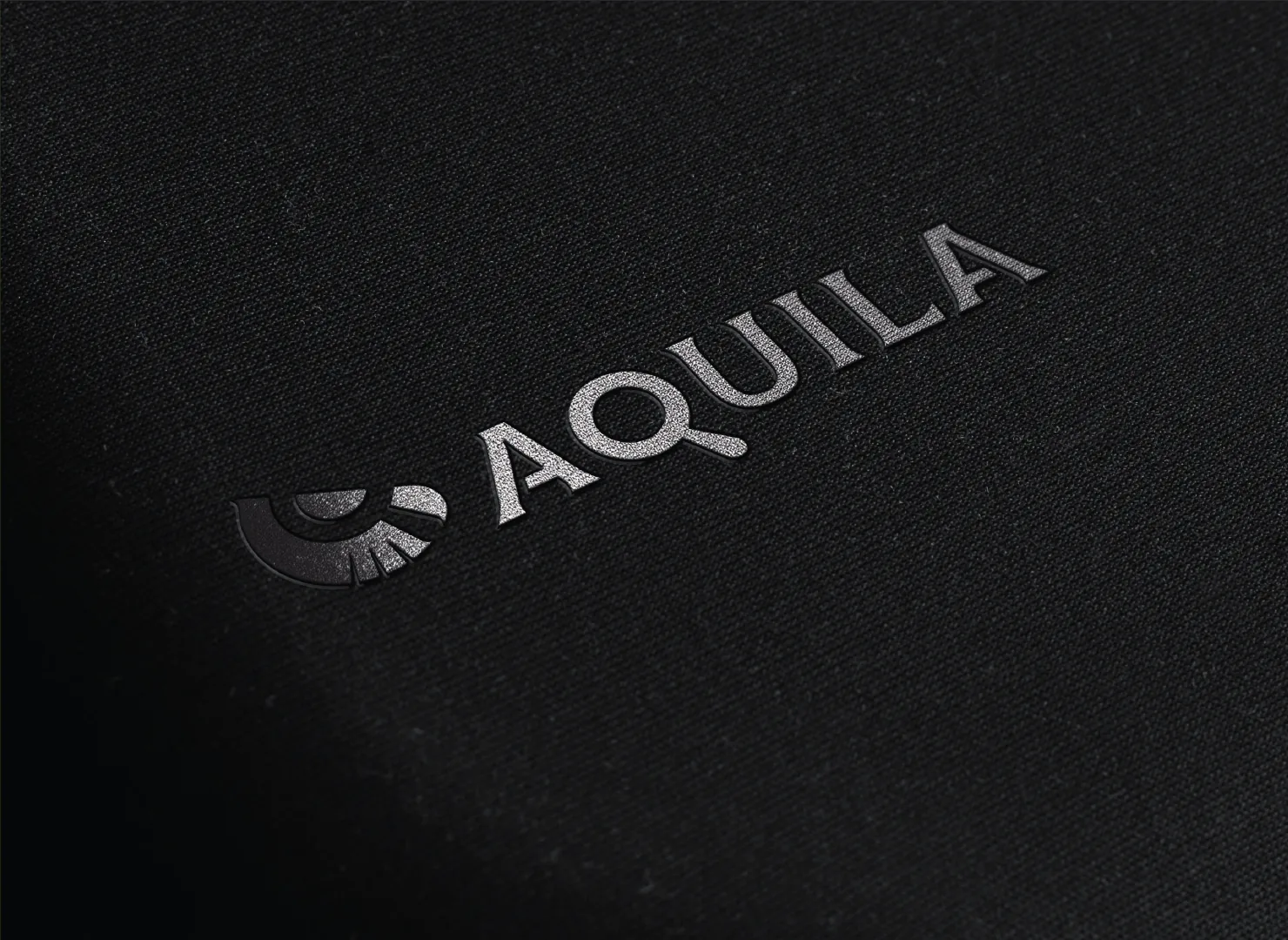 Logotipo da Aquila gravado em tecido escuro.